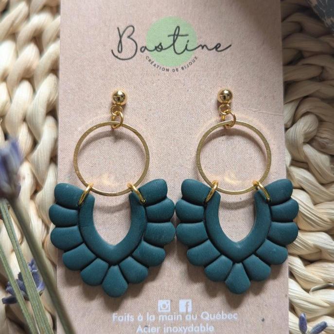 Une paire de Boucles d'oreilles PÉNÉLOPE bleu-vert au design en éventail, accrochées à une carte beige. La carte indique « La Sultana Savonnerie - Création de design » en haut et « Faits à la main au Québec - Acier inoxydable et hypoallergènes » en bas, ainsi que des icônes de médias sociaux pour Instagram et Facebook.