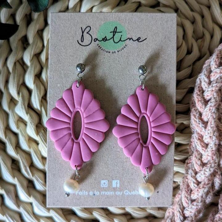 Les boucles d'oreilles REBECCA, en argile rose avec une découpe ovale et des perles nacrées, sont présentées sur une carte de marque étiquetée « La Sultana Savonnerie ». Fabriquée en acier inoxydable hypoallergénique, la carte repose sur une surface tissée à côté d'un tissu tricoté. Le texte au bas indique « Faits à la main au Québec ».