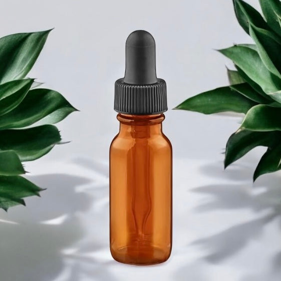 Une petite Bouteille à pipette en verre ambré 15 ml (0,5 oz) de La Sultana Savonnerie, dotée d'un bouchon en caoutchouc noir, est centrée entre deux plantes succulentes vertes sur un fond clair et neutre, la rendant idéale pour conserver des huiles ou des préparations DIY.