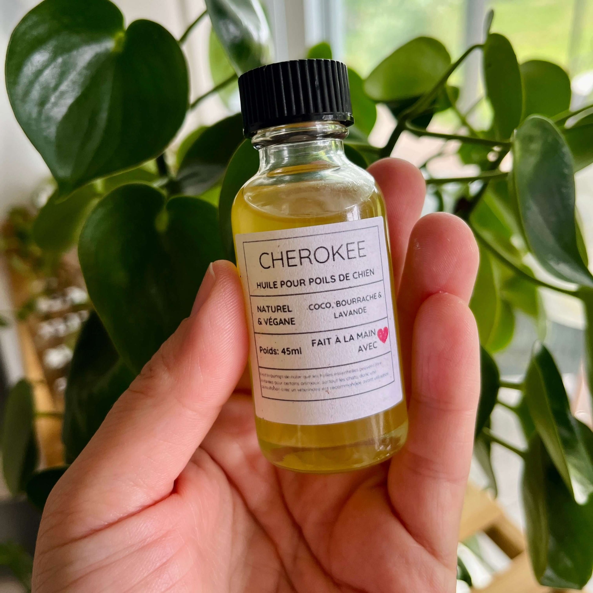 Une main tenant une petite bouteille étiquetée « CHEROKEE ». L'étiquette indique « Huile Pour Poils De Chien », « Naturel & Végan », « Coco, Bourrache & Lavande », « Poids : 45 ml » et « Fait à la Main avec <3 ». Les huiles essentielles de l'Huile régénérante pour chien CHEROKEE sont parfaites pour sublimer le pelage de votre chien. La bouteille vient de La Sultana Savonnerie | Savons et soins naturels faits main | Québec.