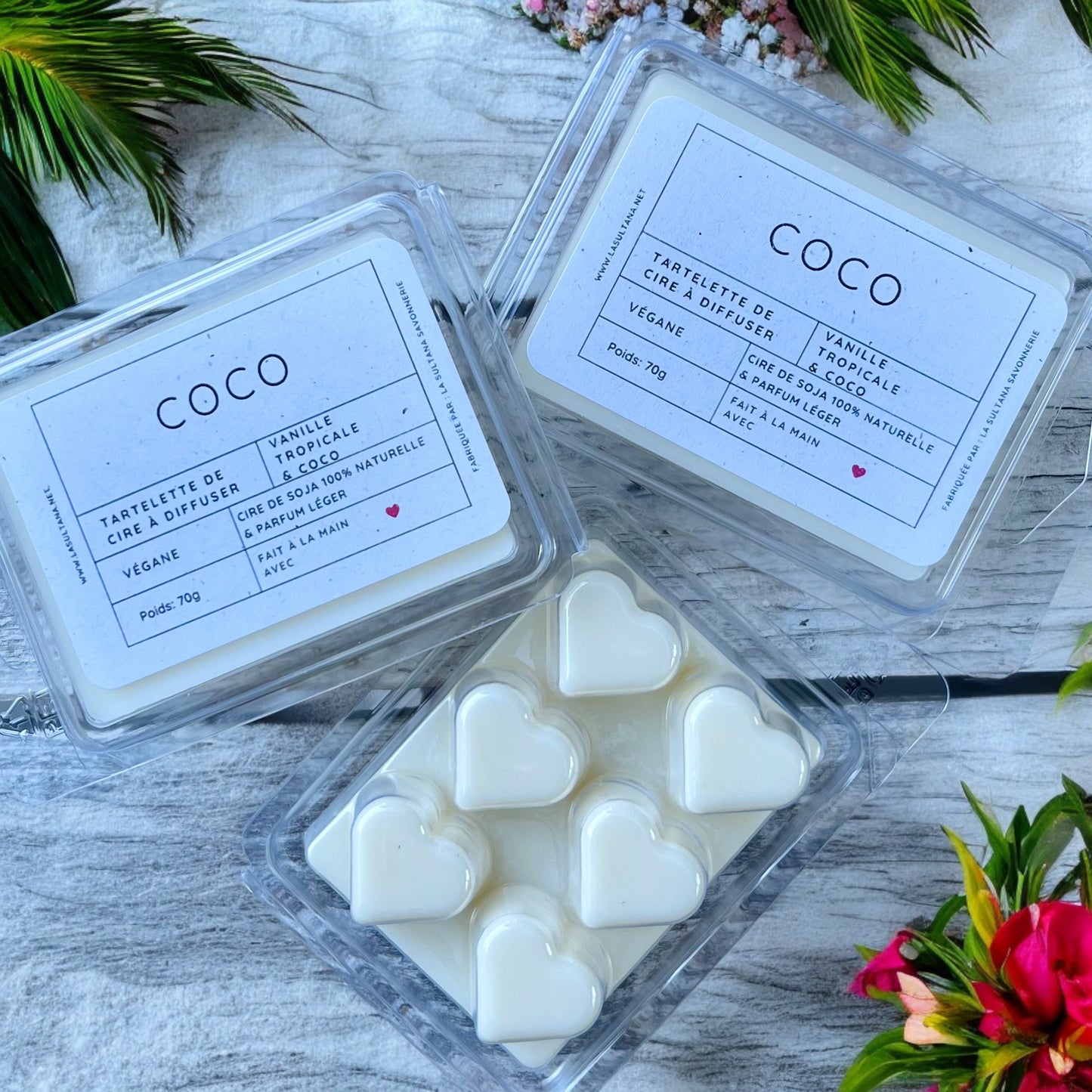 Deux paquets de Tartelette au soja COCO coco et vanille de La Sultana Savonnerie | Savons et soins naturels faits main | Québec sont présentés sur une surface en bois. L'emballage souligne que ces fondants de cire naturels faits à la main ont un parfum de vanille. Il y a quelques feuilles vertes et des fleurs dans les environs.