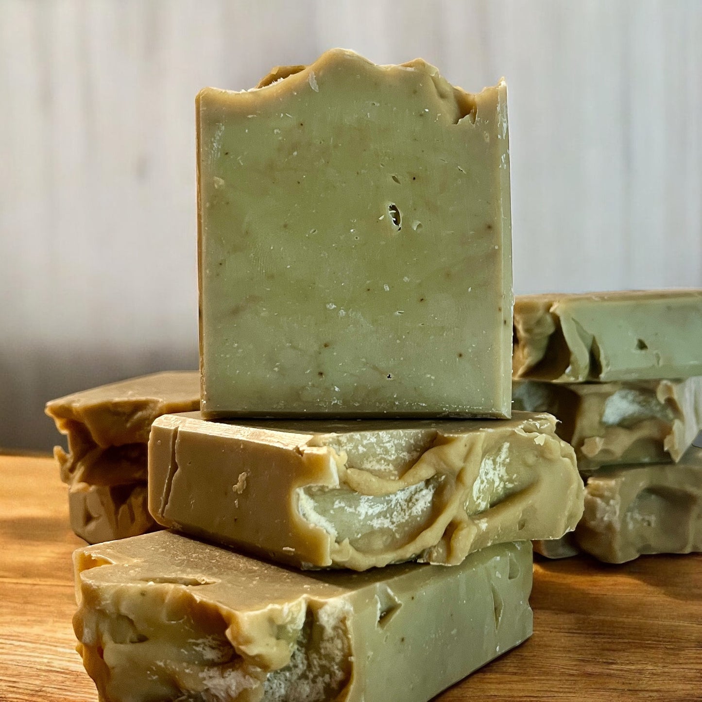 Une pile de Savon IMPARFAIT à l'huile d'olive, myrrhe et musc de La Sultana Savonnerie | Savons et soins naturels faits main | Québec repose sur une surface en bois. Le savon présente une couleur naturelle et terreuse avec une texture légèrement rugueuse, complétée par des imperfections visibles et un aspect rustique. Son charme authentique est mis en valeur sur le fond légèrement flou.